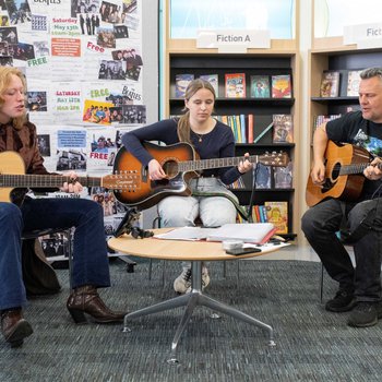 3 people sat in library playing instruments