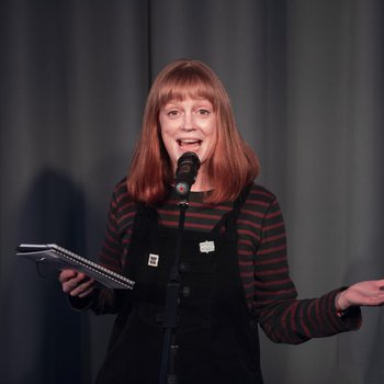 Lady on stage holding a book and reciting into a microphone