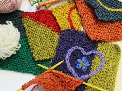 Care squares made out of different coloured yarns on a table with knitting needles