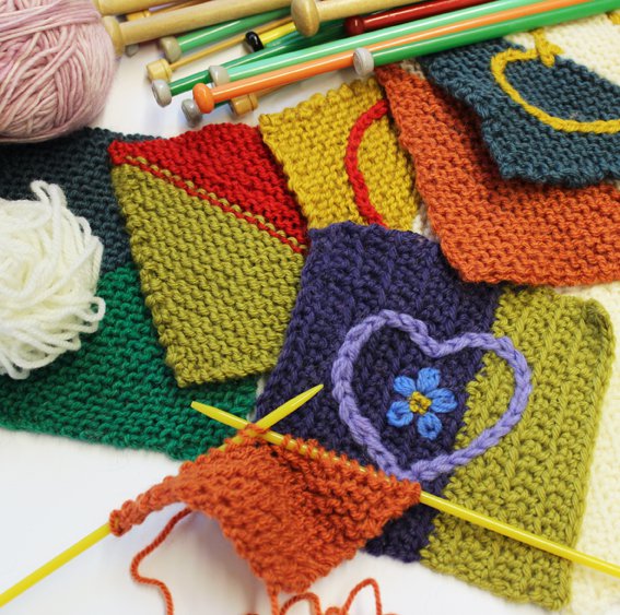 A selection of knitted and crochet squares, one is embellished with a chain stitch heart and tiny blue flower.