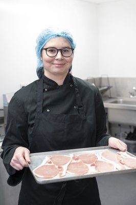 An Inspire College student in a chef uniform and hairnet, holding a tray of bacon.