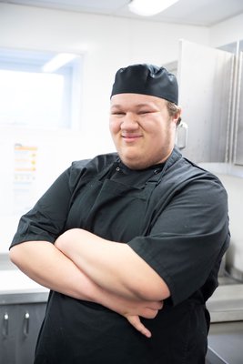 Inspire College Learner wearing black chef's uniform, smiling with his arms folded.