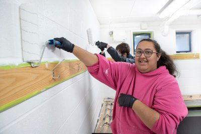 An Inspire College learner in a pink hoodie painting a wall.