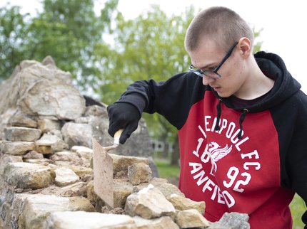 A young person building a brick wall outside.