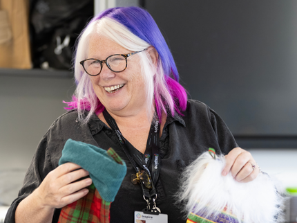 A white woman with colourful dyed hair holds two handmade Christmas stockings