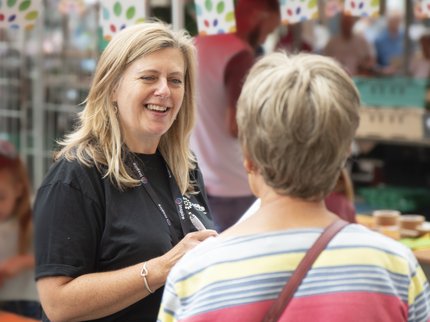 A woman from Inspire speaking to a customer at a market stall outside