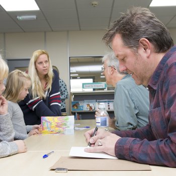 An author in a checked blue and red shirt sign his book for a young person