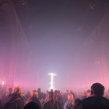 People standing in a dark church with pink light flooding to the ceiling.