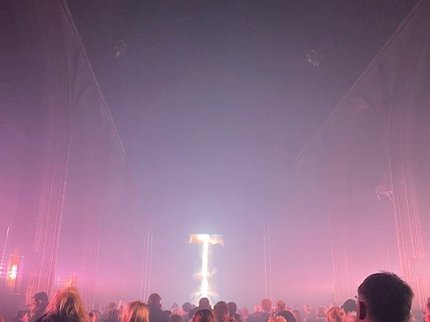 People standing in a dark church with pink light flooding to the ceiling.