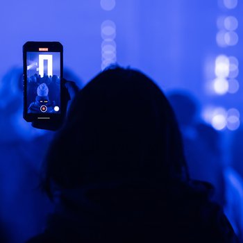 Back of head holding a mobile phone in a dark church with light installations.