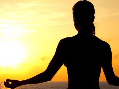 Silhouette of woman meditating in front of the sun