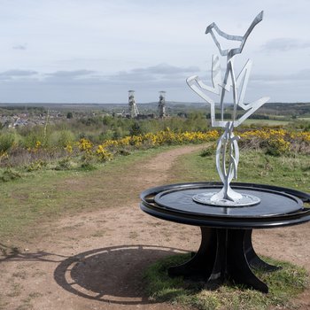 A metal casted sculpture at Vicar Water Country ark with mining towers in the bakground