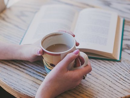 a book open on a table and somebody holding onto a mug of tea
