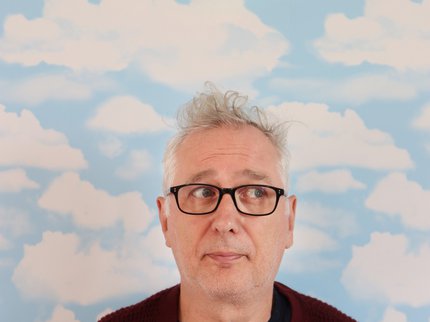 A white man wearing black rimmed glasses and a red jumper looking up to the sky.