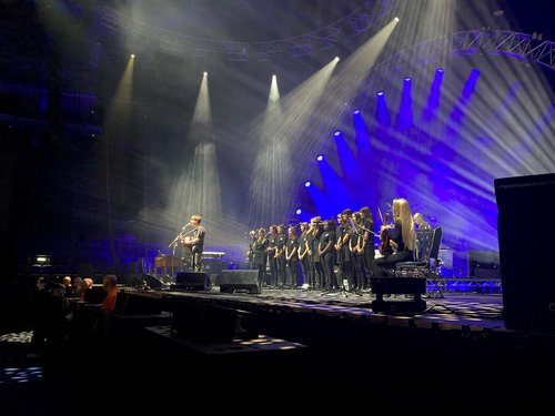 The school choir on stage with Jake Bugg, lit by blue stage lights.