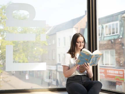 woman sat reading book in the window of library