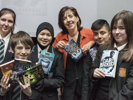 An author stands with a group of school children who are holding up her book