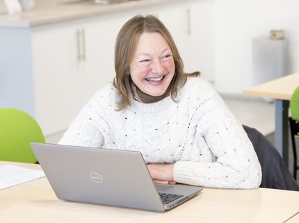 A woman with blonde hair sat in front of a laptop smiling