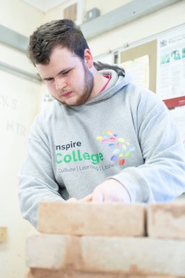 An Inspire College learner in a hoodie, building a brick wall.