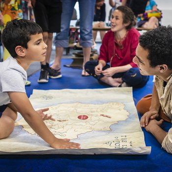 children and adults sat on the floor looking at a map.