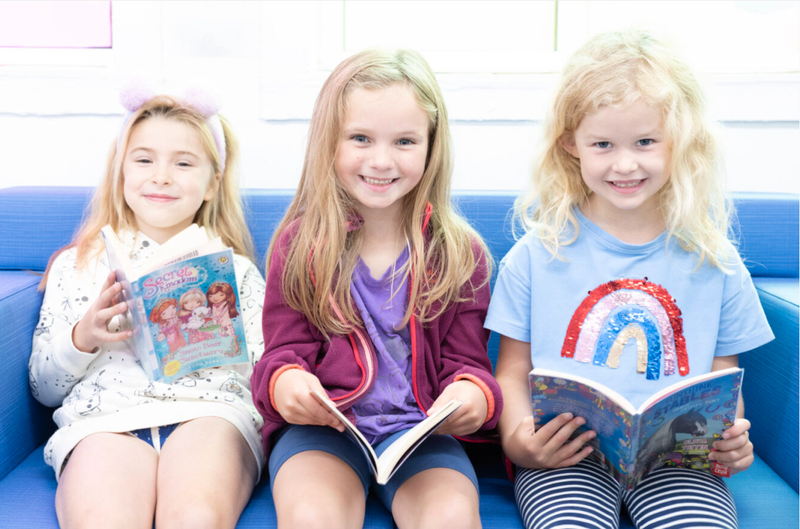 Three girls sitting on a bench in the library smiling and holding books