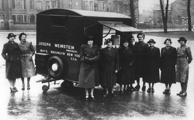 A group of women standing next to a vintage car during world war two