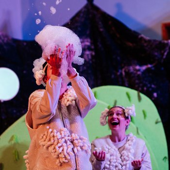 Two performers dressed as sheep, with white woolly costumes and curly headpieces, are playing with bubbles.