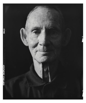 An elderly man looking at the camera with a black background