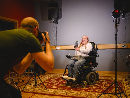A photographer taking a photo of a girl using a wheelchair and holding a remote