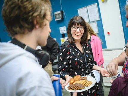 A woman with short brown hair offering a plate of biscuits to a boy and smiling.