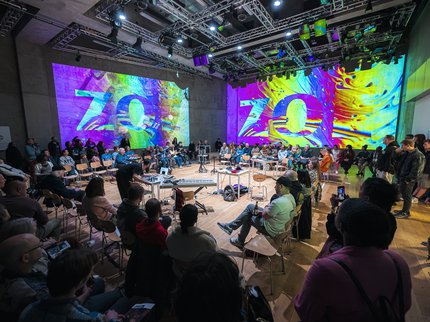A photo from the Unlocked 2025 event at Nottingham Contemporary. Photo is taken from behind the audience awith a view of the wohle room inlcuding the audience stage area and digital graphics on the walls of the room.