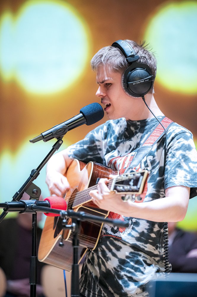 A man playing the guitar and singing with headphones on