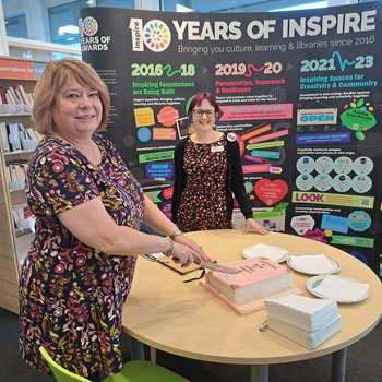A woman cutting a cake in front of an exhibition