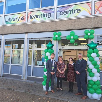 Four people stood outside a library in front of a balloon arch