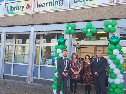 Four people stood outside a library in front of a balloon arch