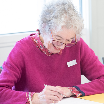 Learner in a pink jumper writing at a desk.