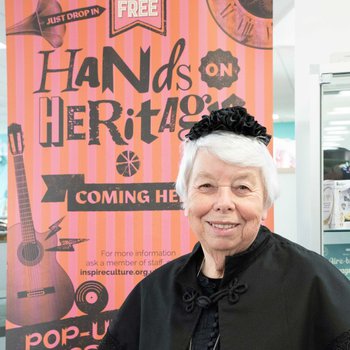 Women dressed up in old clothes stood in front of Hands on Heritage banner