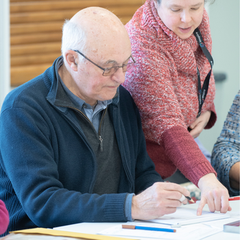 Learner wearing a blue zip- up hoodie receiving help from tutor wearing a pink cardigan.