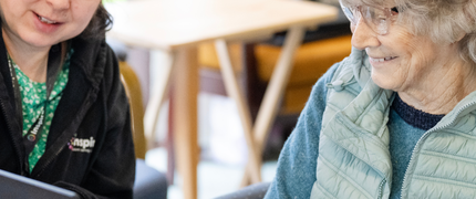 A tutor sits with an older lady during a digital skills course. The tutor points at a laptop screen.