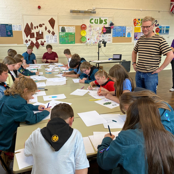 Peter Snelling from MyPockets leading a workshop. A group of children (cubs) sit around a table drawing intently.