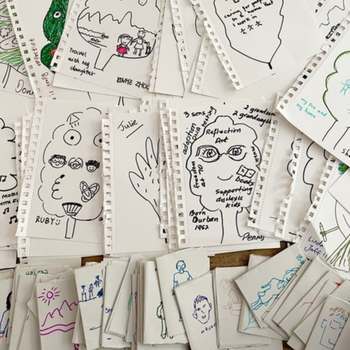 A table full of drawings from the workshops. On each piece of paper there's a leaf drawn, with annotations about the artist's life.