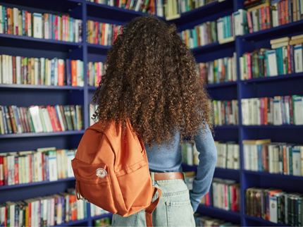 A person with their back to the camera wearing an orange backpack looks at a shelf of books