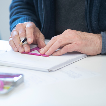 Learner's hands using a protractor at a desk.