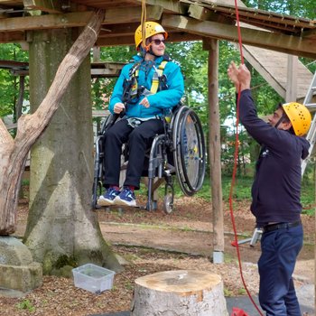 Staff member being lifted by ropes in a wheelchair.
