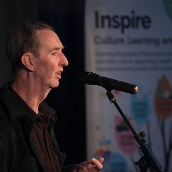 Gentleman on stage holding a book and reciting into a microphone