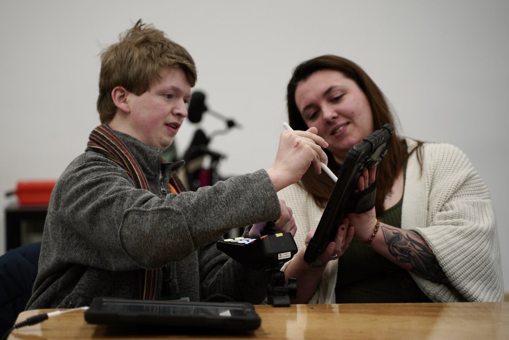 A young person is drawing on a iPad supported by an artist