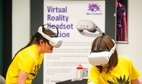 Two people wearing VR headsets and yellow T Shirts.