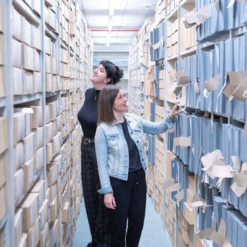 Two people walking between shelves at Nottinghamshire Archives, fascinated at the documents beside them