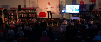 Wide shot image showing an author talking to a group of people in a library