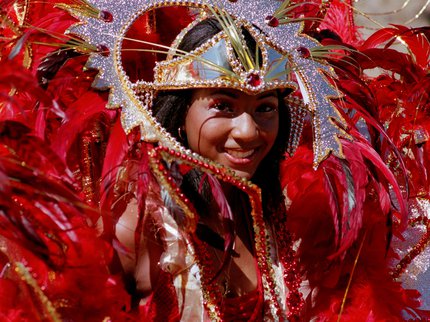 A lady smiling wearing traditional carnival dress of red feathers with sequins and glitter